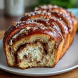 Festive King Cake Cinnamon Babka Loaf with rich cinnamon swirl, creamy cheese layer, and vibrant purple, green, and gold decorations.  