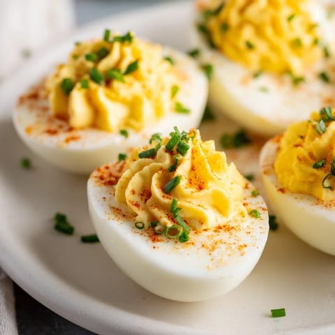 Twelve golden halved eggs filled with smooth, tangy yolk mixture on a white serving plate.