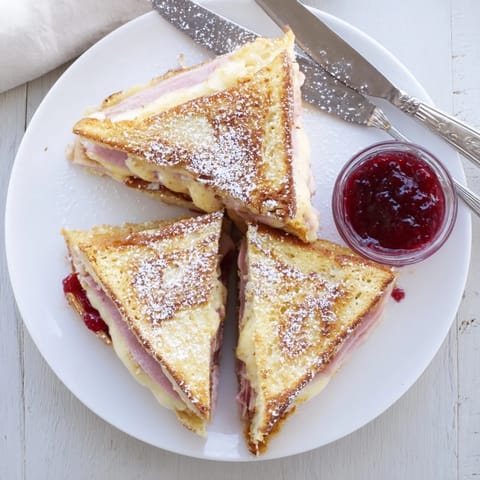 Monte Cristo sandwich dipped in egg batter and pan-fried, featuring crispy edges, savory ham, and gooey Swiss cheese on white bread.