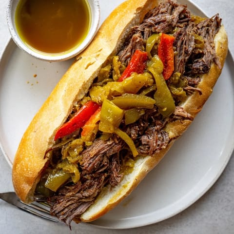 Chicago-style Italian Beef Sandwich with tender slow-cooked beef, peppers, and tangy giardiniera, served hot with dipping jus.