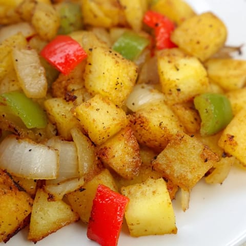 Sizzling Home Fries with crispy edges and sweet peppers, served alongside eggs for a hearty breakfast.