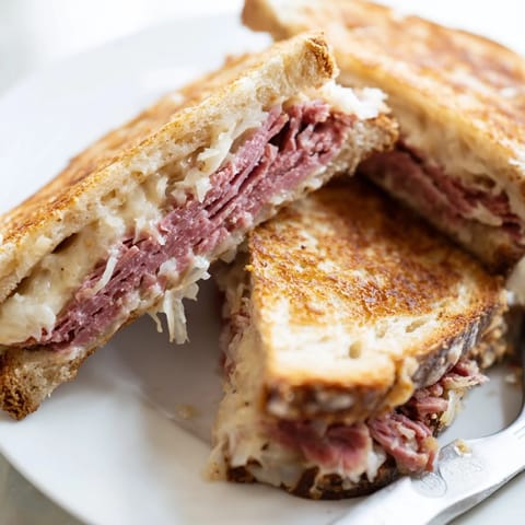 Griddled Reuben Sandwich on rye bread overflowing with juicy corned beef, Russian dressing, and melted Swiss cheese on a plate.