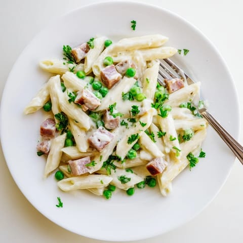 Steaming bowl of Spring Pea & Ham Pasta garnished with fresh parsley, showcasing vibrant green peas and golden ham bits.