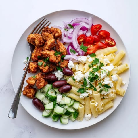 A serving of Crispy Chicken Greek Pasta features feta crumbles and fresh parsley garnish.