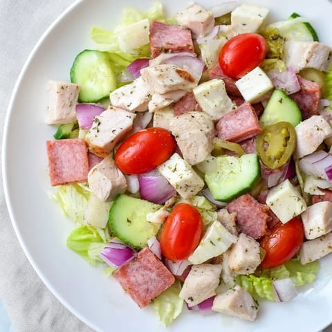 Bright Italian Deli Chopped Chicken Salad served in a rustic bowl with juicy tomatoes and crunchy cucumbers, ready for a quick lunch or vibrant dinner alongside a glass of Pinot Grigio.