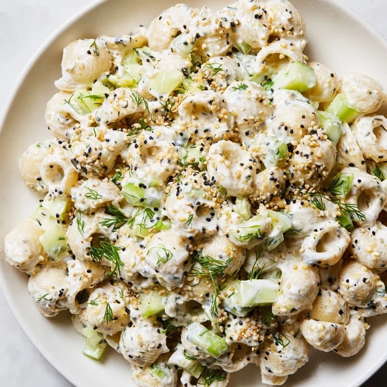 A chilled bowl of Cucumber Crunch Pasta Salad, featuring tiny shell pasta, crunchy cucumbers, and green onions, finished with aromatic dill and savory seasoning.