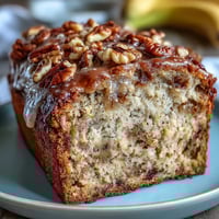 A slice of high-protein banana bread with Greek yogurt, golden brown and moist, topped with chopped walnuts and dark chocolate chips.